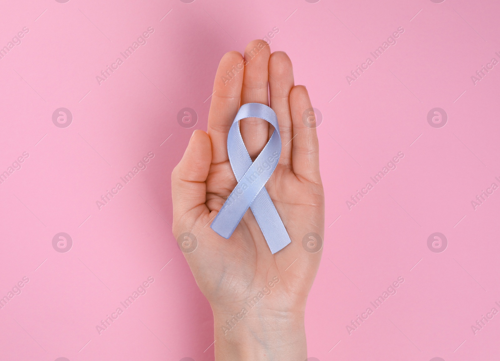 Photo of International Psoriasis Day. Woman with light blue ribbon as symbol of support on pink background, top view
