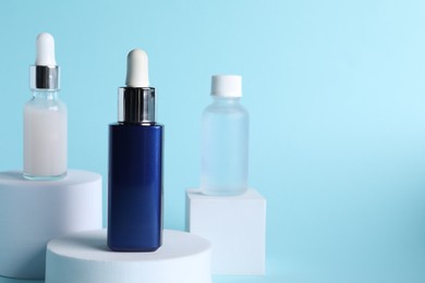 Bottles of cosmetic serum on light blue background, space for text