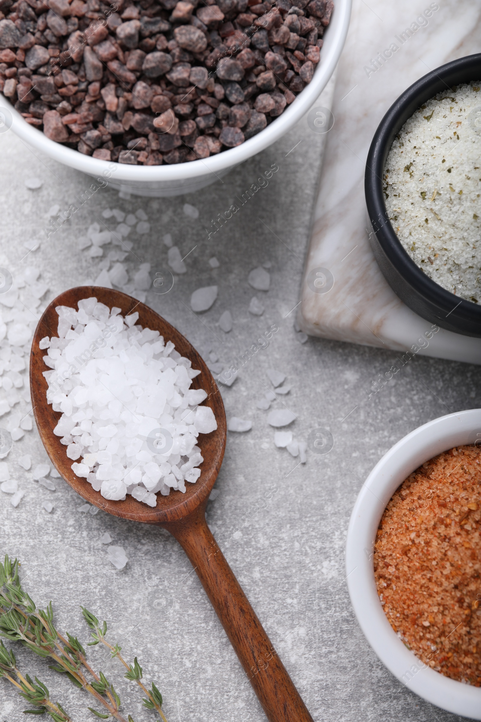 Photo of Different kinds of salt on grey table, flat lay