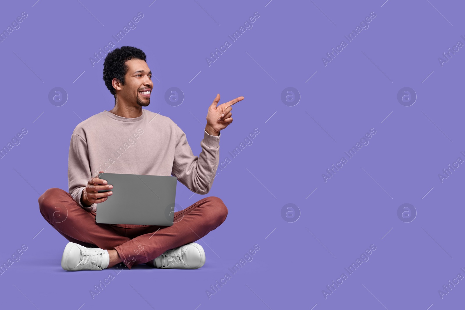 Photo of Happy man with laptop pointing at something on purple background. Space for text