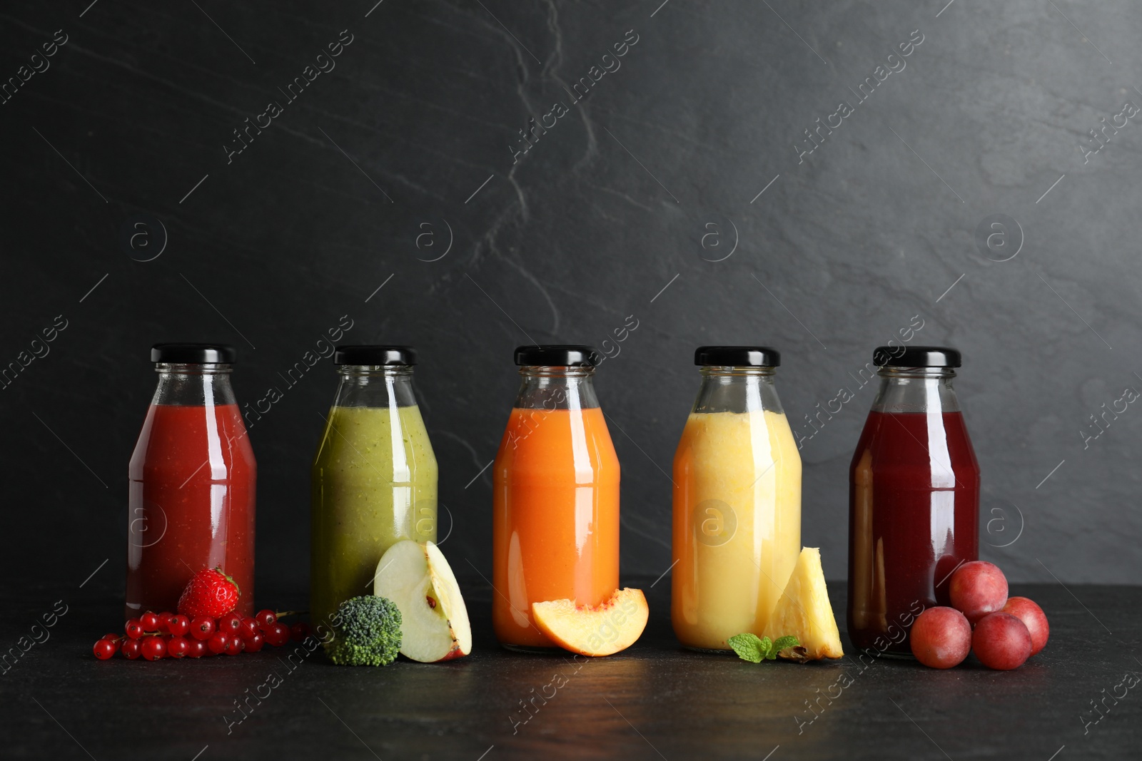 Photo of Bottles with delicious colorful juices and fresh ingredients on black table