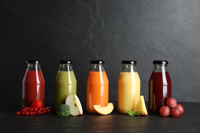 Bottles with delicious colorful juices and fresh ingredients on black table