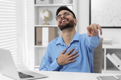 Photo of Handsome young man laughing while pointing at something in office