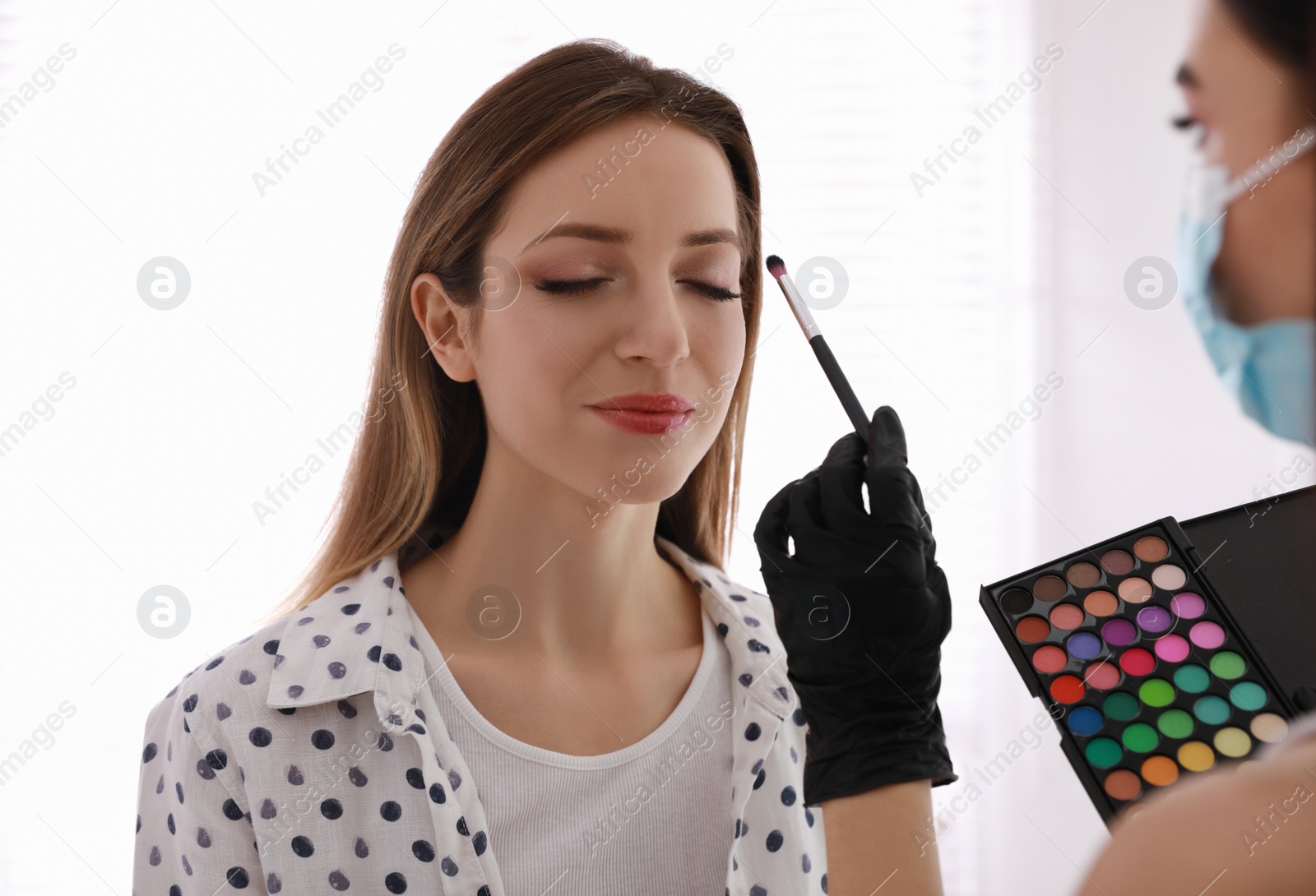 Photo of Makeup artist in protective mask and gloves working with woman indoors. Preventive measures during COVID-19 pandemic