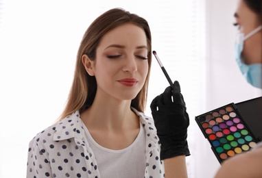 Photo of Makeup artist in protective mask and gloves working with woman indoors. Preventive measures during COVID-19 pandemic