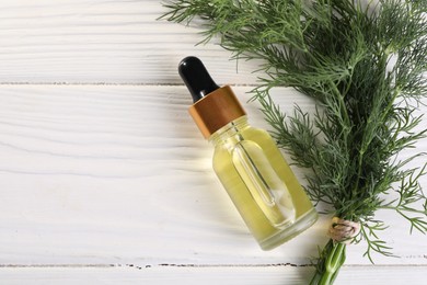 Bottle of essential oil and fresh dill on white wooden table, flat lay. Space for text