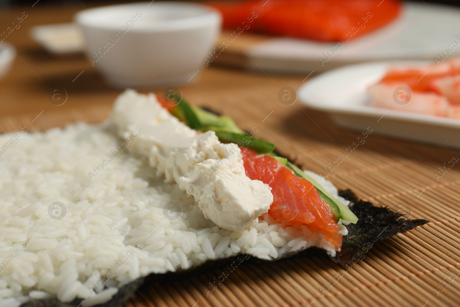 Photo of Unwrapped sushi roll with rice, cucumber, cheese and salmon on bamboo mat, closeup