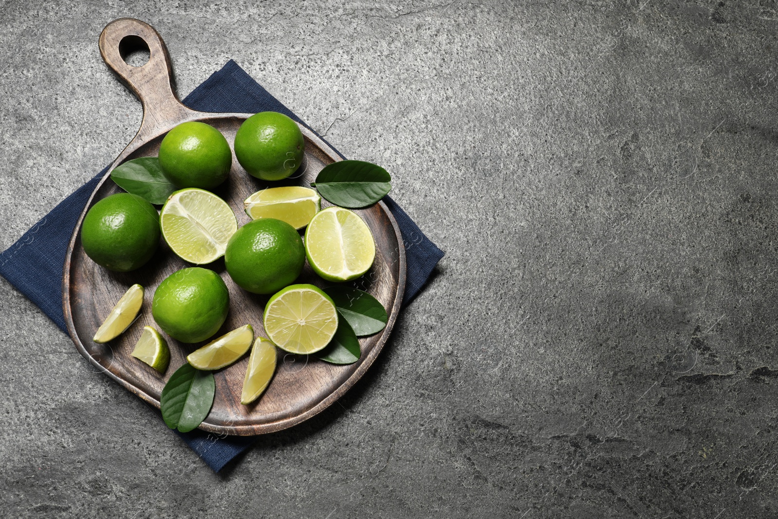 Photo of Fresh ripe limes and leaves on grey table, top view. Space for text