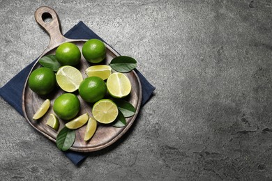 Fresh ripe limes and leaves on grey table, top view. Space for text