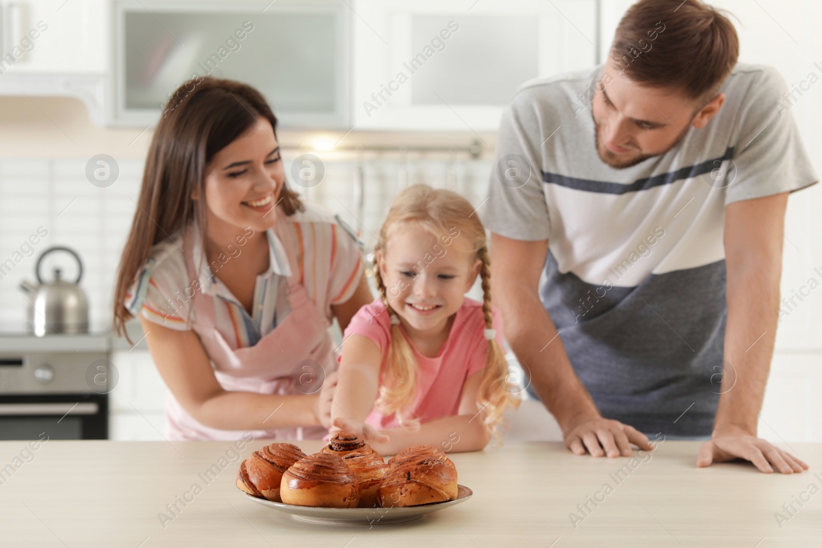 Photo of Happy family with freshly oven baked buns at table in kitchen