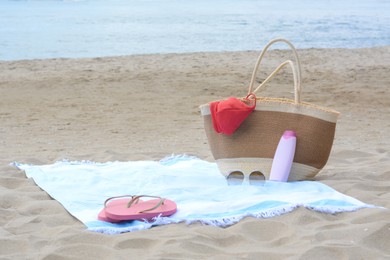 Light blue striped towel with bag, flip flops, sunglasses and sunblock on sandy beach