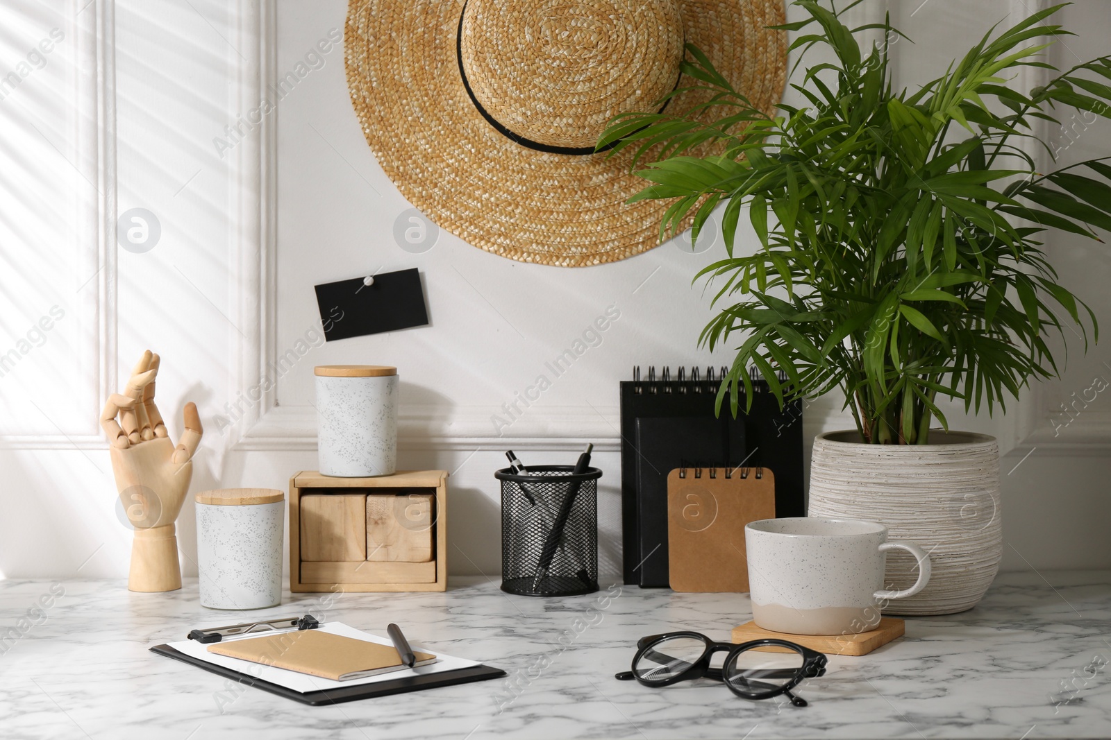 Photo of Stylish office workplace. Decor elements, glasses, cup and stationery on marble table near white wall