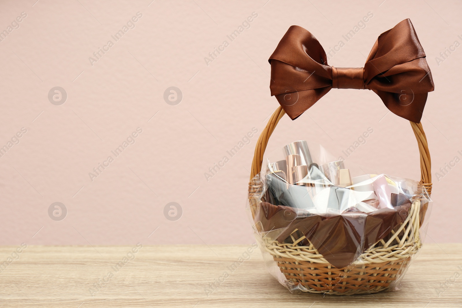 Photo of Wicker gift basket with cosmetic products on wooden table. Space for text