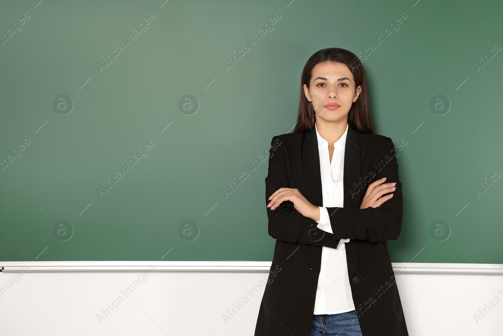 Photo of Young teacher standing at blackboard in classroom. Space for text