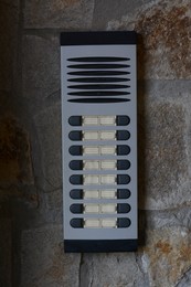 Photo of Modern intercom on concrete wall with stone fragments. Security system