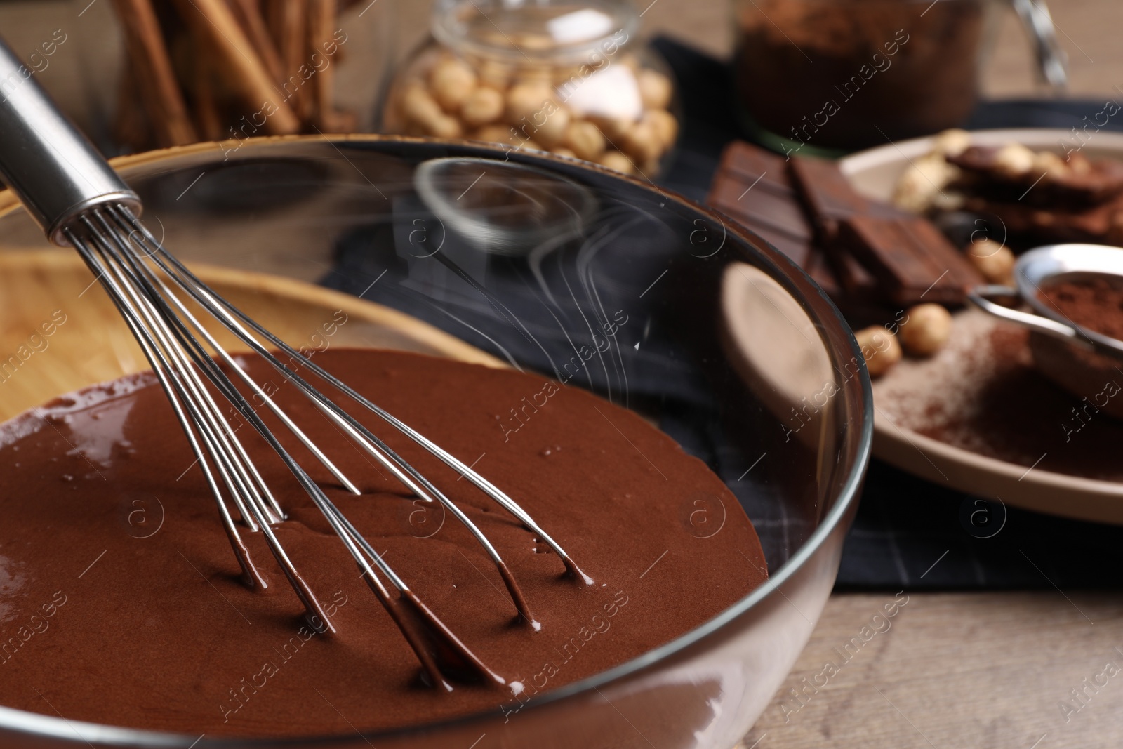 Photo of Bowl of chocolate cream with whisk on wooden table, closeup