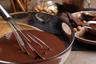 Bowl of chocolate cream with whisk on wooden table, closeup