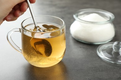 Photo of Woman stirring sugar in tea at grey table, closeup