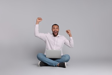 Happy young man with laptop on grey background, space for text