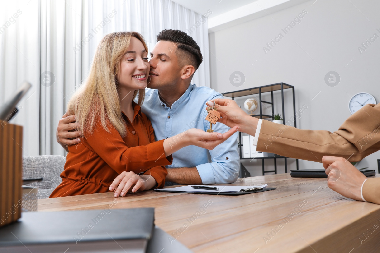Photo of Real estate agent giving house key to couple at table in office