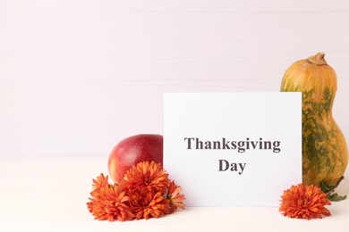 Photo of Thanksgiving day, holiday celebrated every fourth Thursday in November. Card, apple, pumpkin and chrysanthemum flowers on white wooden table, space for text
