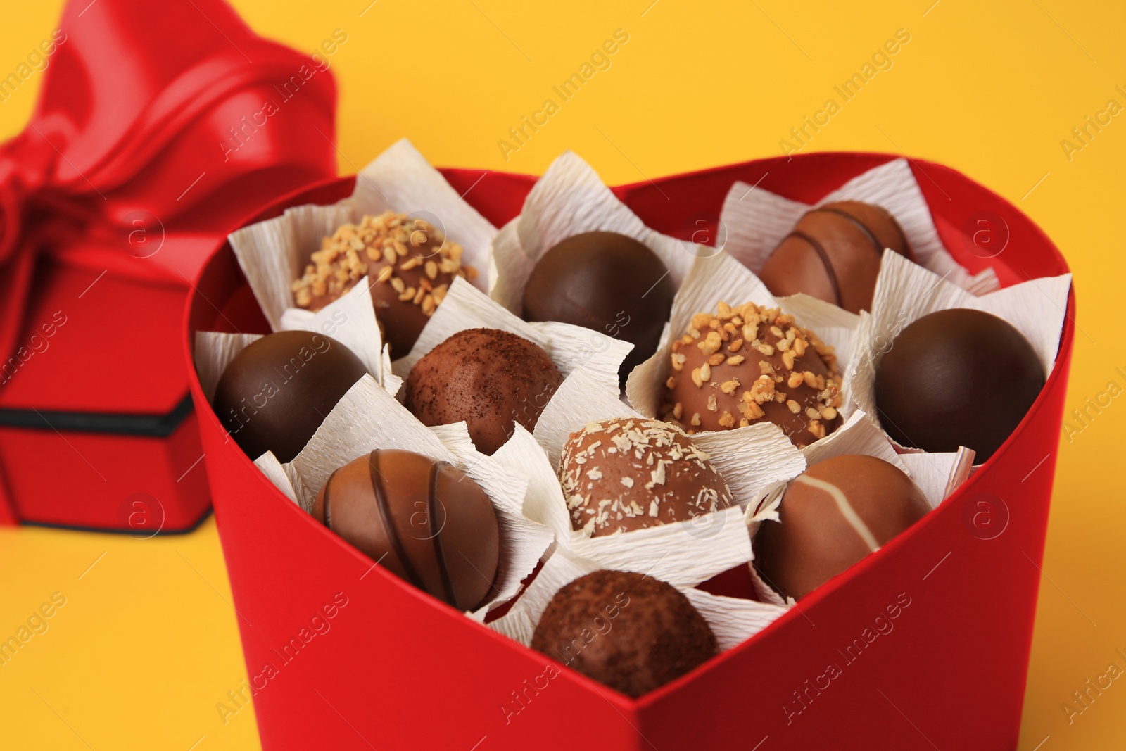 Photo of Heart shaped box with delicious chocolate candies on yellow background, closeup