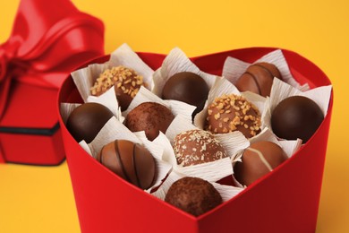 Photo of Heart shaped box with delicious chocolate candies on yellow background, closeup