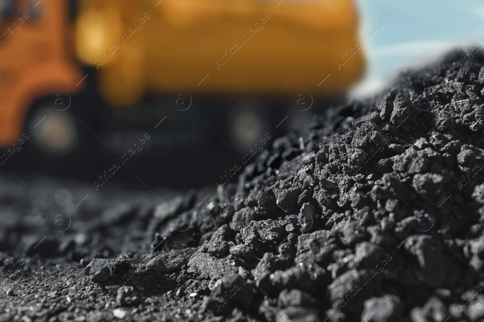 Image of Pile of coal and blurred yellow truck on background, closeup
