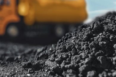 Pile of coal and blurred yellow truck on background, closeup