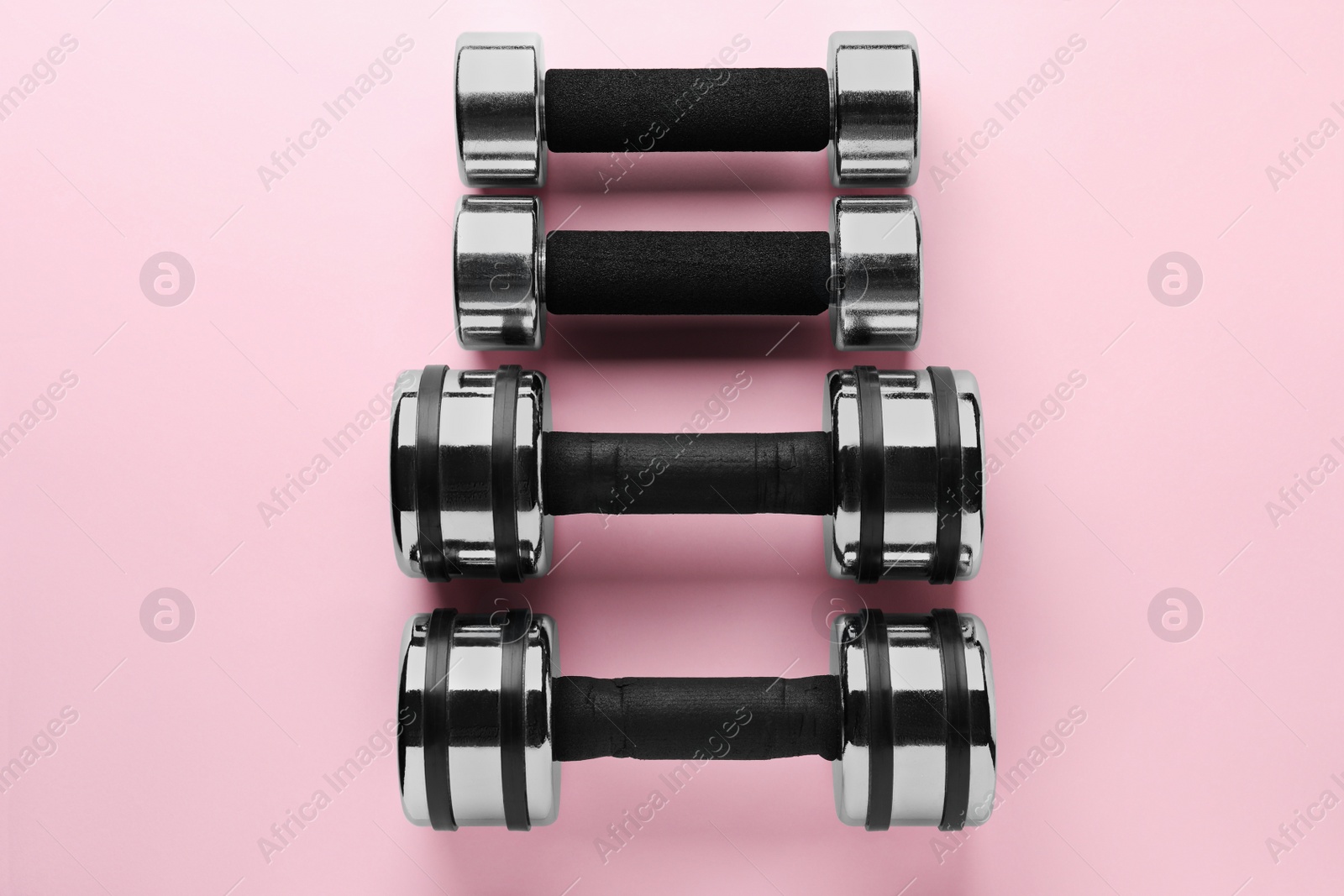 Photo of Dumbbells on light pink background, flat lay. Weight training equipment