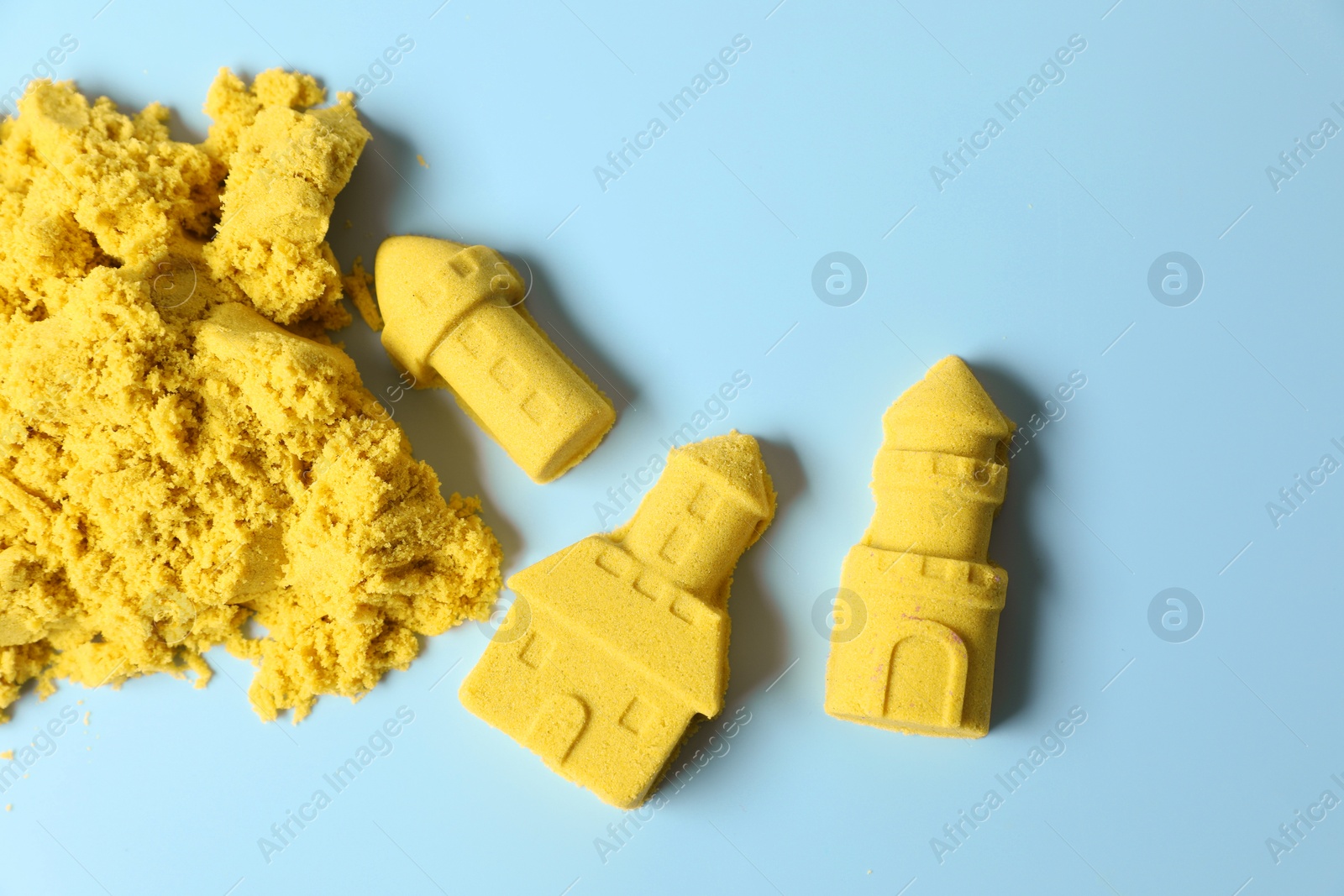 Photo of Castle figures made of yellow kinetic sand on light blue background, flat lay