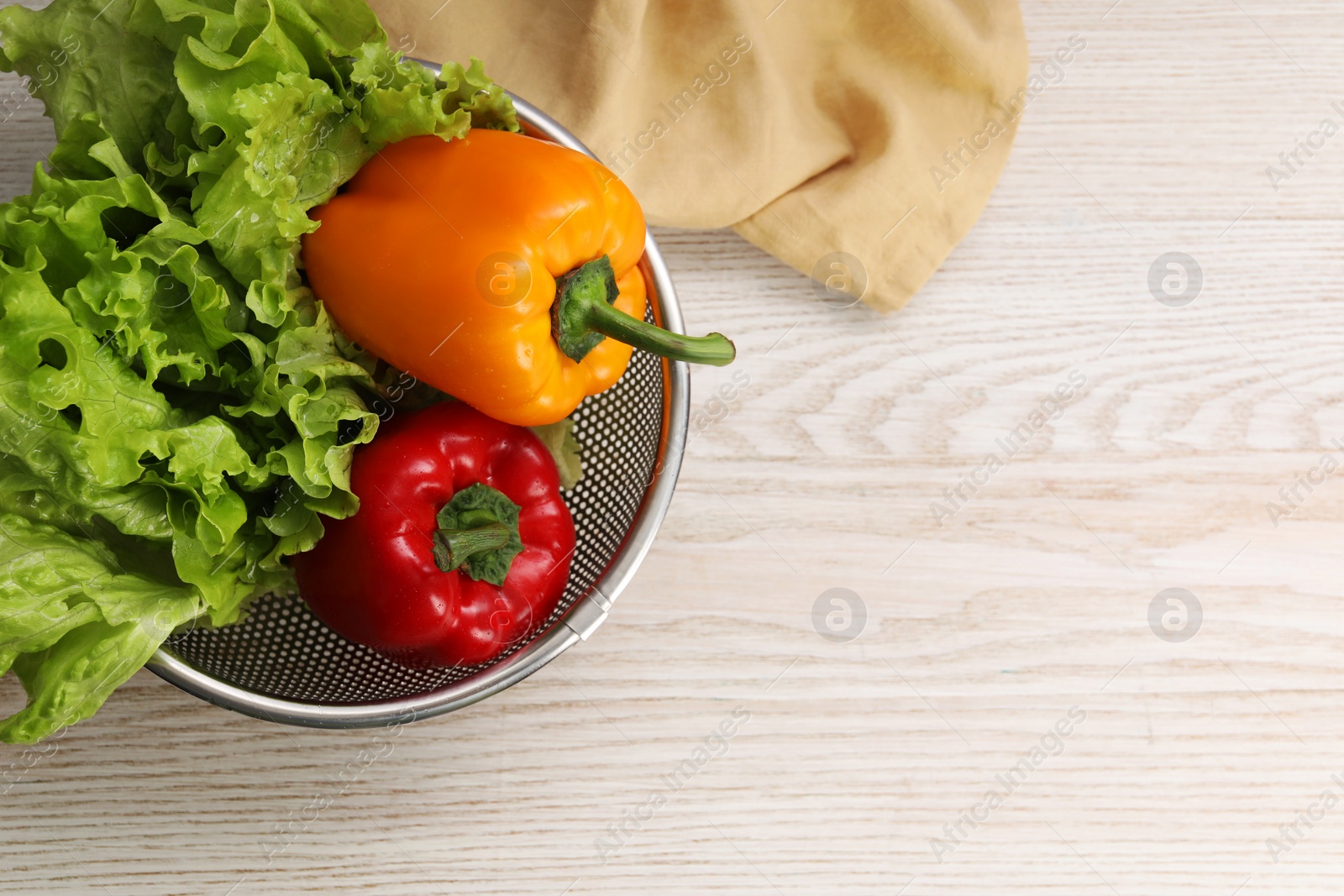 Photo of Colander with fresh lettuce and bell peppers on wooden table, top view. Space for text