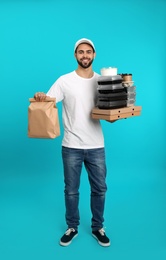 Young courier with pizza boxes, containers and drinks on color background. Food delivery service