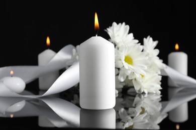 Photo of White chrysanthemum flowers and burning candles on black mirror surface in darkness, closeup. Funeral symbols