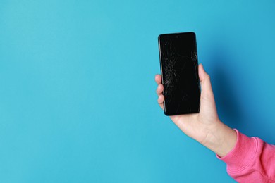 Woman holding damaged smartphone on light blue background, closeup with space for text. Device repairing