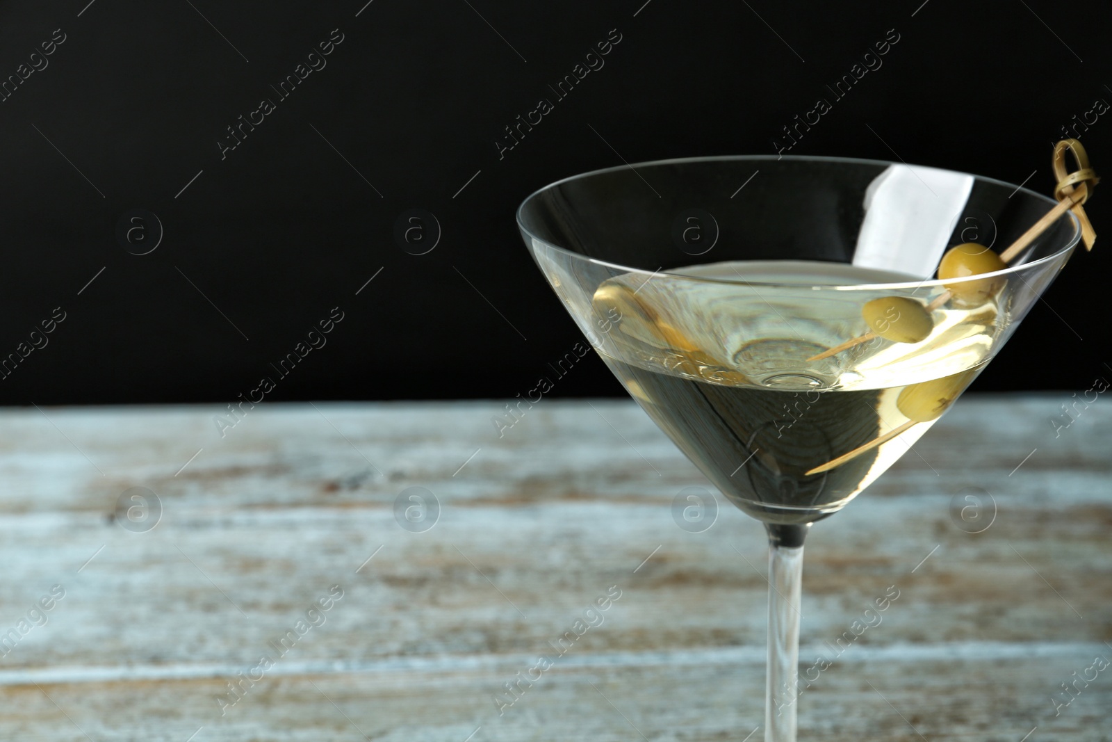 Photo of Glass of Classic Dry Martini with olives on wooden table against black background, closeup. Space for text