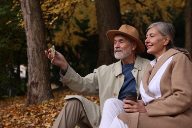 Affectionate senior couple taking selfie in autumn park