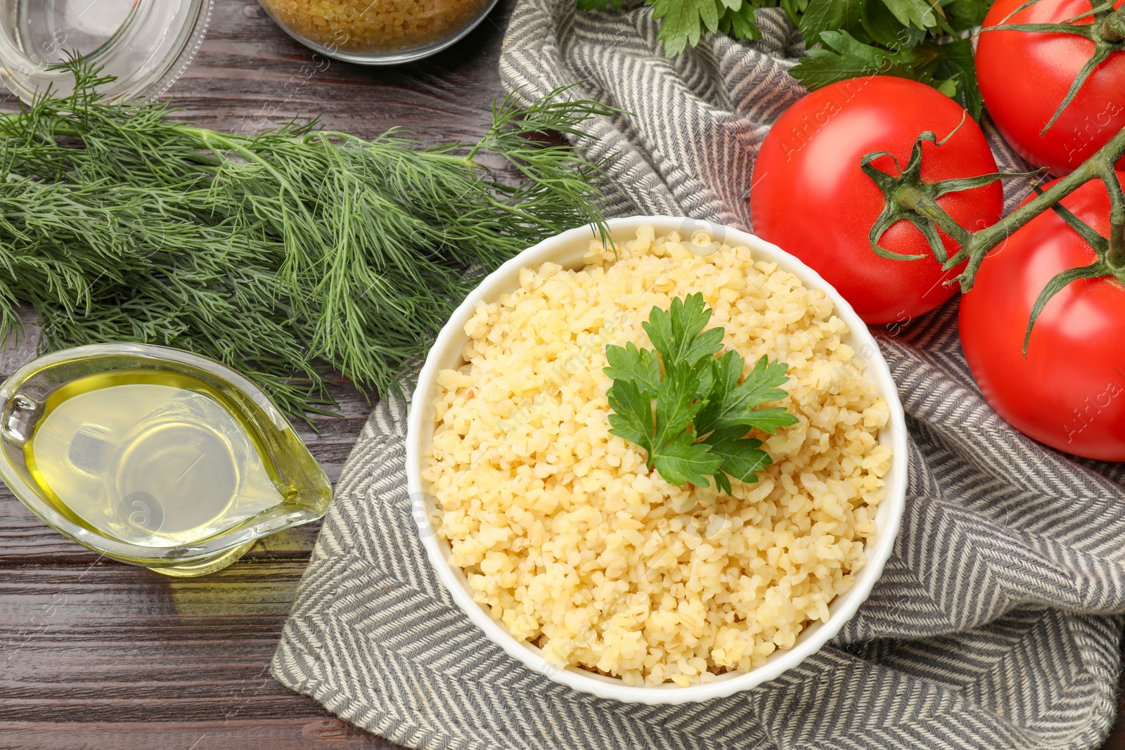 Photo of Delicious bulgur with greens, tomatoes and oil on wooden table, flat lay