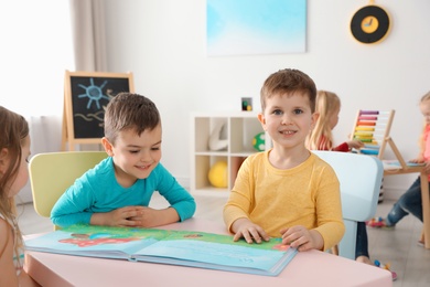 Photo of Cute little children reading book together at table indoors. Learning and playing