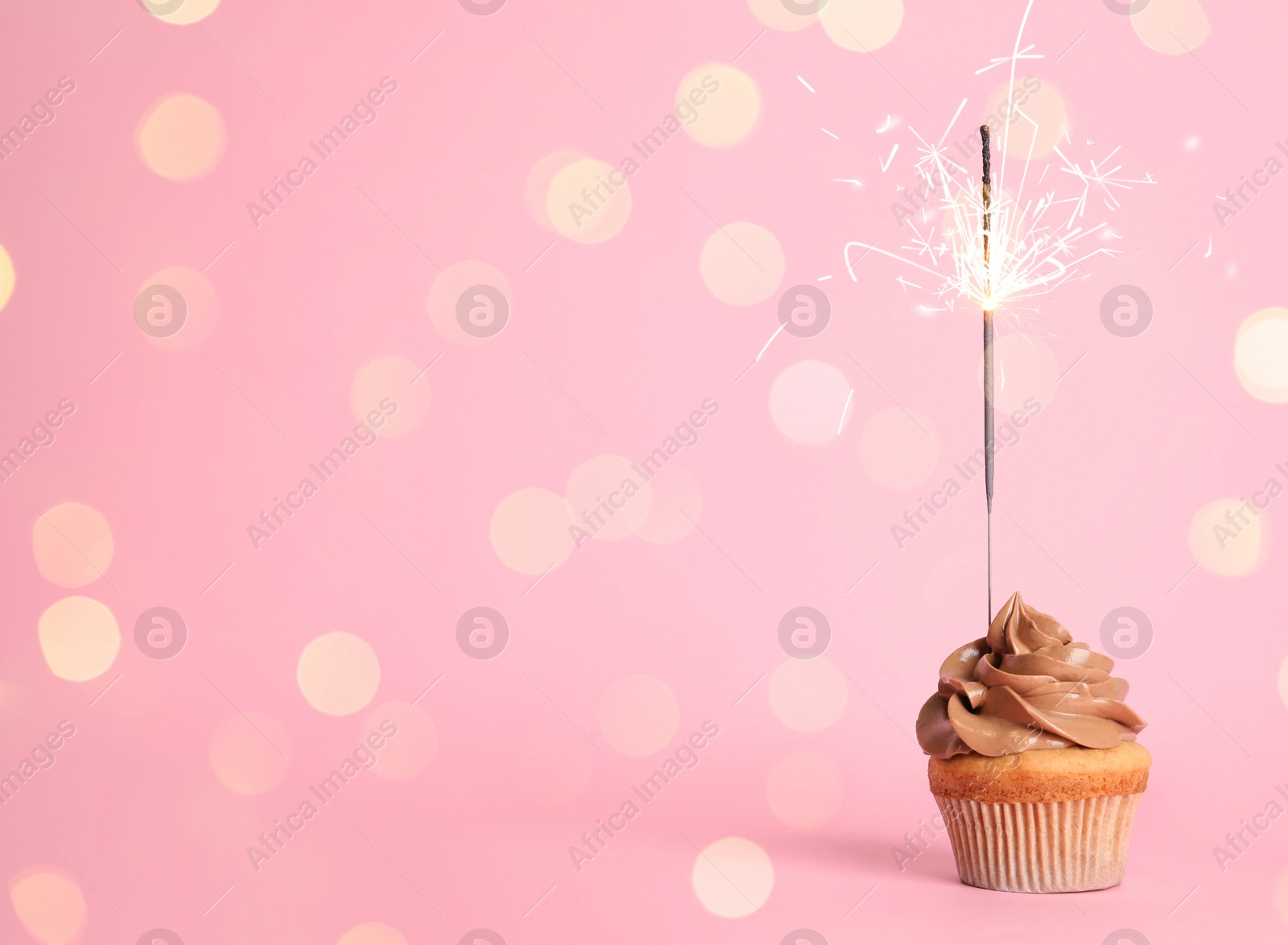 Image of Birthday cupcake with sparkler on pink background. Space for text