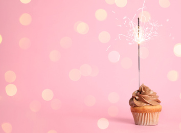 Image of Birthday cupcake with sparkler on pink background. Space for text