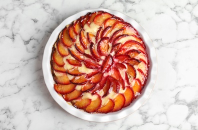 Photo of Delicious cake with plums on white marble table, top view