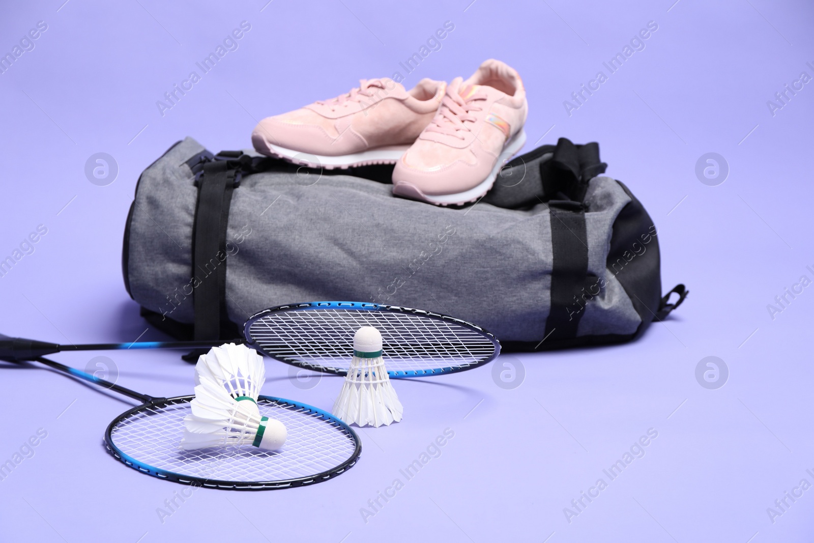 Photo of Feather badminton shuttlecocks, rackets, bag and sneakers on violet background