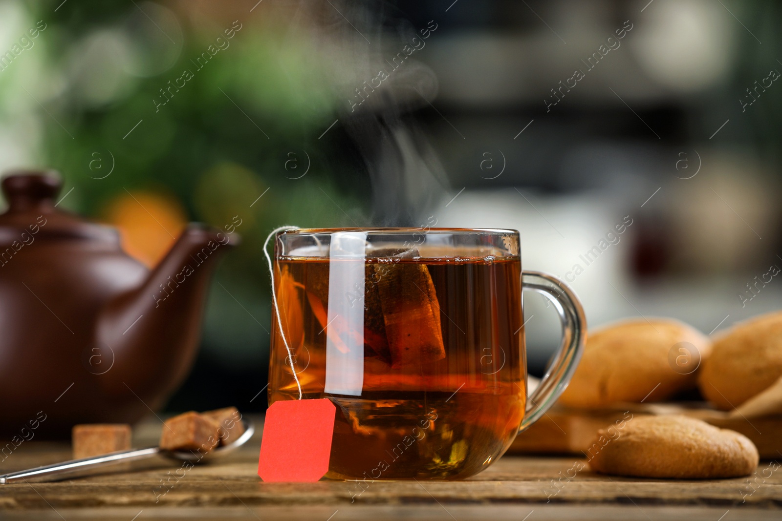 Photo of Tea bag in glass cup of hot water and cookies on wooden table against blurred background