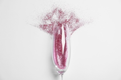 Photo of Champagne glass with pink glitter on white background, top view. Hilarious celebration