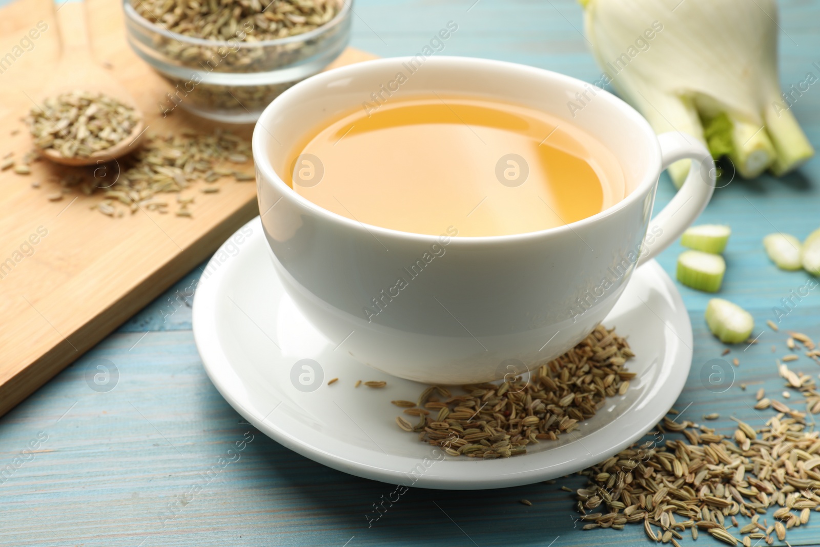 Photo of Fennel tea in cup, seeds and fresh vegetable on light blue wooden table, closeup