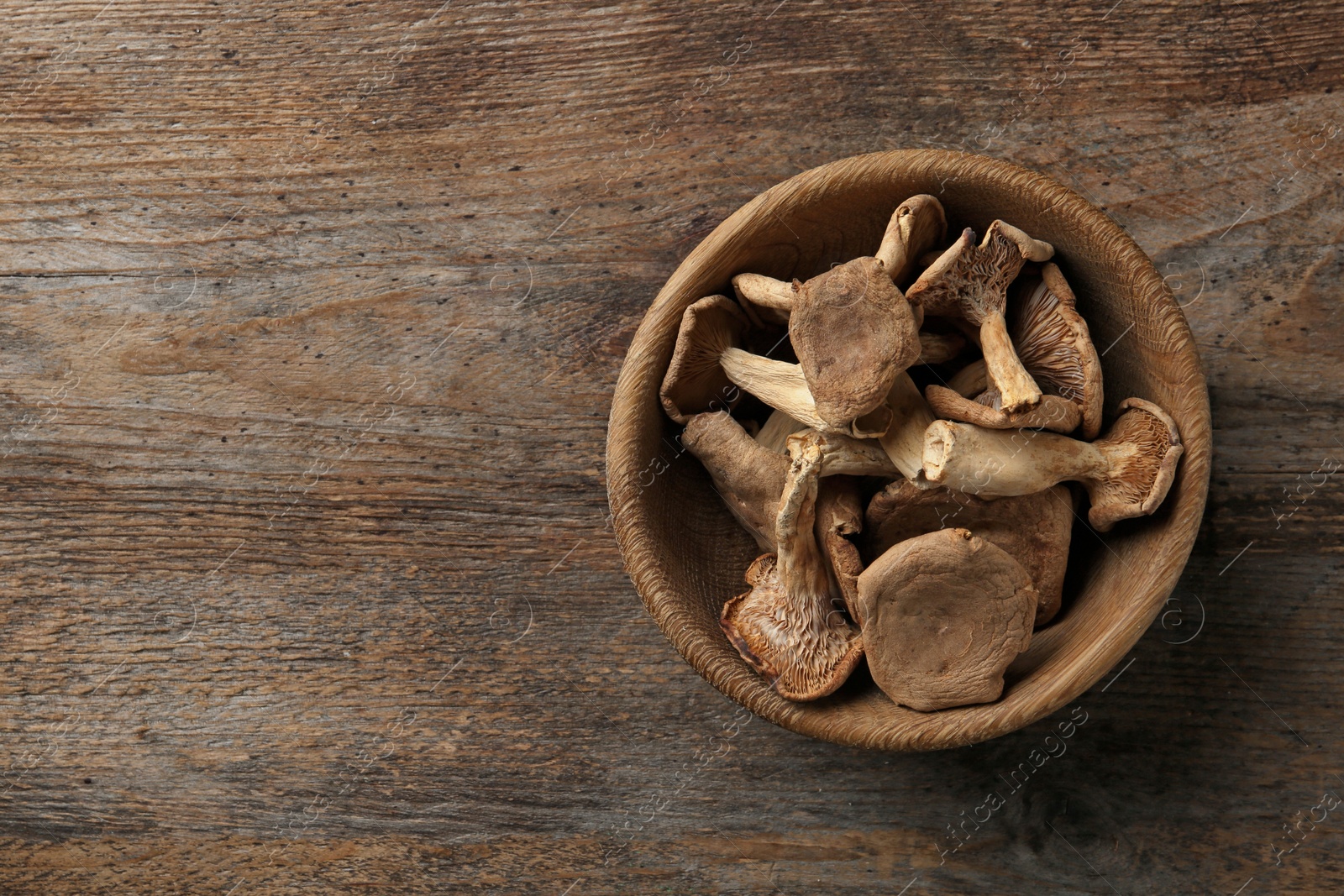 Photo of Bowl of dried mushrooms on wooden background, top view with space for text