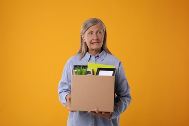 Photo of Confused unemployed senior woman with box of personal office belongings on orange background