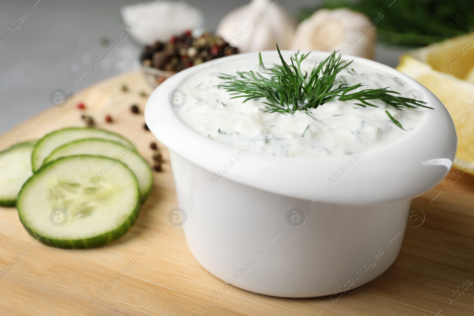 Photo of Bowl with cucumber sauce on wooden board