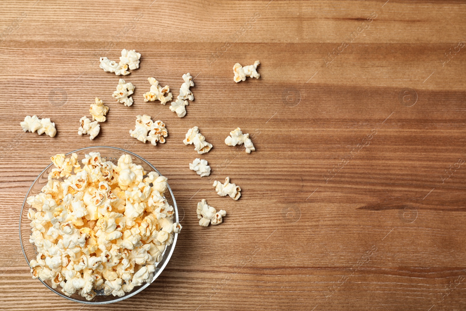 Photo of Glass bowl with tasty popcorn on wooden background, top view. Space for text